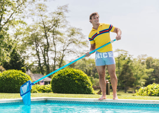 Man standing outside by pool wearing yellow polo and grey slim fit boxers with words "NICE" on the front in white bold font.
