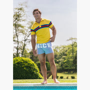 Man standing outside by pool wearing yellow polo and grey slim fit boxers with words "NICE" on the front in white bold font.