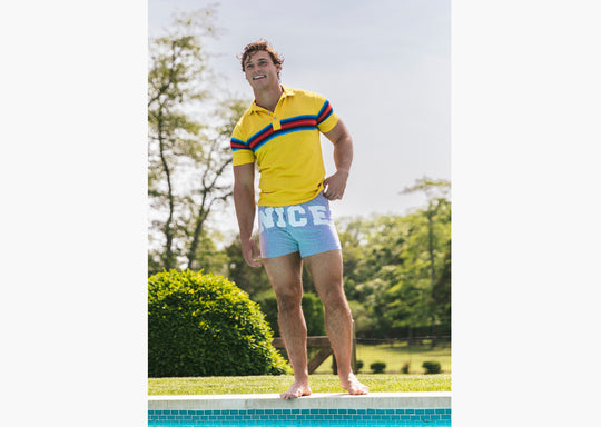 Man standing outside by pool wearing yellow polo and grey slim fit boxers with words "NICE" on the front in white bold font.
