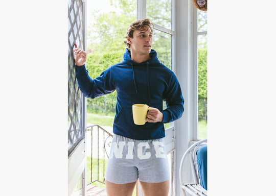 Man standing inside of house wearing navy blue sweatshirt and grey slim fit boxers with words "NICE" on the front in white bold font.