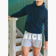 Man standing inside of house on stairs wearing navy blue sweatshirt and grey slim fit boxers with words "NICE" on the front in white bold font.