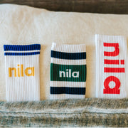 three pairs of crew socks with "nila" on them in various colors tucked into a bed