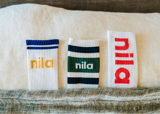 three pairs of crew socks with "nila" on them in various colors tucked into a bed