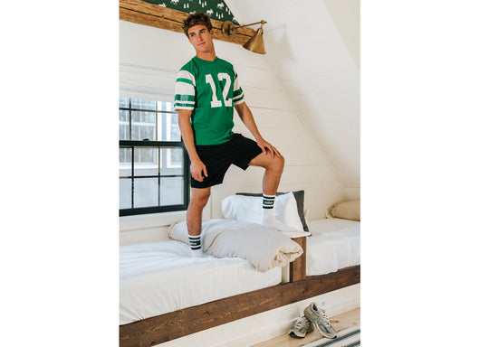 Man standing on bed wearing green jersey and white/green crew socks with letters Nila on them
