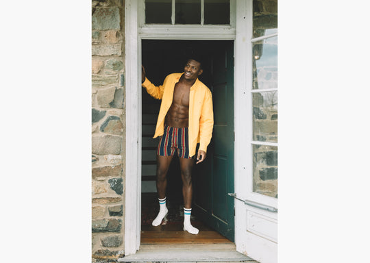 Man wearing yellow/red/blue stripe slim fit boxers and an open yellow dress shirt.