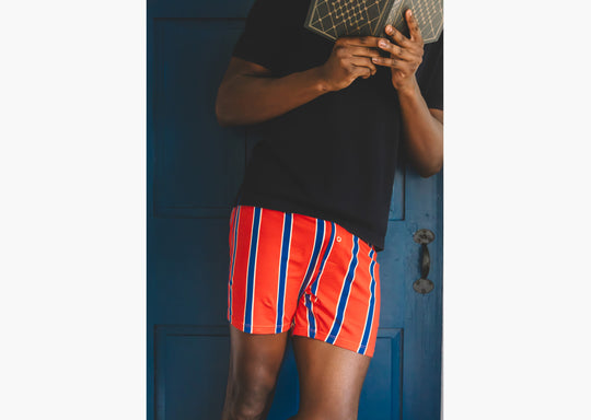 Man holding book wearing black shirt and red/blue/yellow stripe slim fit boxers.