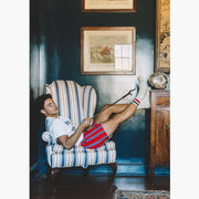 Man sitting on chair wearing red/blue/yellow stripe slim fit boxers and red/blue crew socks.