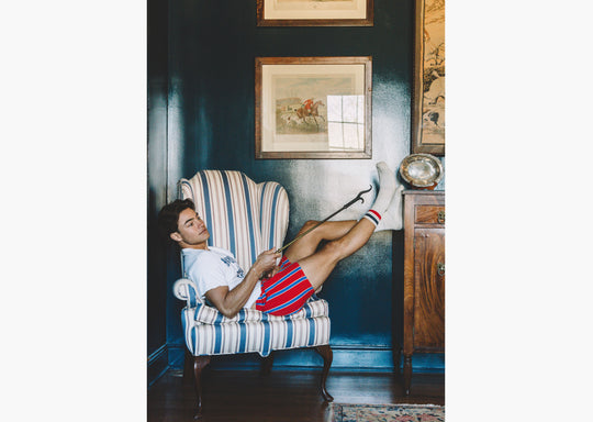 Man sitting on chair wearing red/blue/yellow stripe slim fit boxers and red/blue crew socks.
