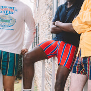 Three man standing together each wearing various colored striped slim fit boxers.