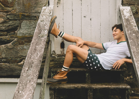 Man sitting on wooden steps wearing white shirt, boots and green slim fit boxers with white dots.