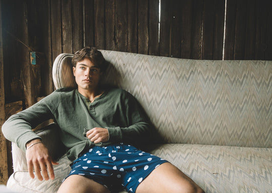 Man sitting on couch wearing green long sleeve shirt and blue slim fit boxers with white dots.