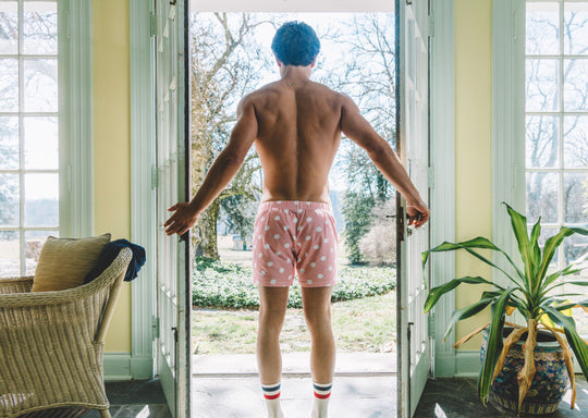 Back shot of shirtless man opening a door wearing pink slim fit boxers with white dots.