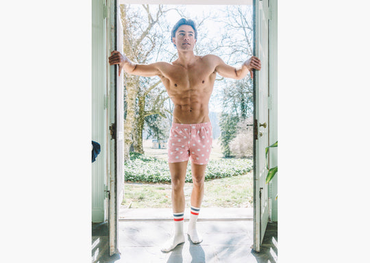Front shot of shirtless man walking into doorway wearing pink slim fit boxers with white dots 