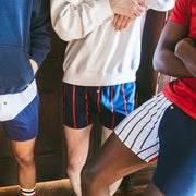 Close up shot of 3 men standing in a group all wearing "Navies" slim fit boxer. Two are red/white/blue striped while 1 has blue/red. All three have gold button. One man is wearing navy hoody, one white hoodies, and one red shirt.
