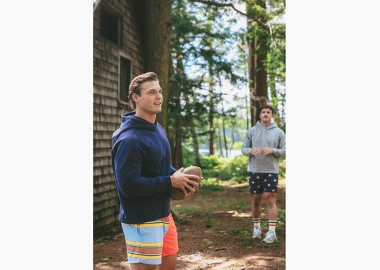 Man holding football wearing navy hoodie in forest