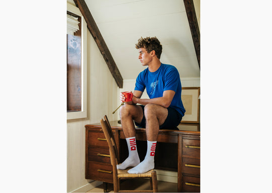 Man sitting on desk wearing blue shirt and white crew socks with letters "nila" in red.