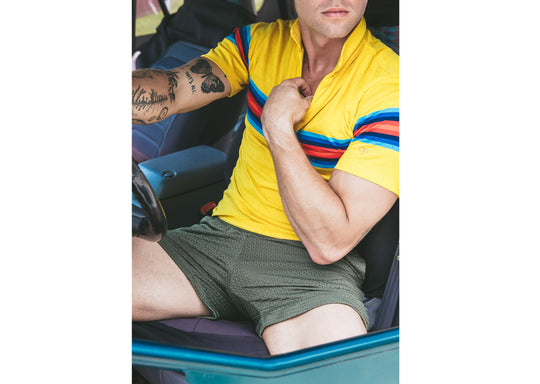 Man sitting in car wearing yellow polo and olive lounge shorts.