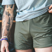 Man with tattoos wearing grey shirt and olive mesh shorts.