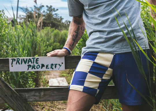 Man wearing half checkered half solid blue and white mesh lounge shorts sitting on a sign that says private property.