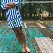 Man standing on tennis court with arms crossed wearing blue and white cabana stripe hoodie and lounge shorts.