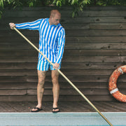 Man cleaning a pool wearing blue and white cabana stripe hoodie and lounge shorts.