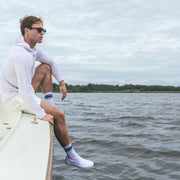 Man sitting by edge of boat with feet over water wearing linen stripe hoodie.