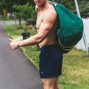 Shirtless man wearing navy blue lounge shorts with A monogram standing next to a road.