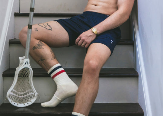 Man sitting shirtless on stairs wearing navy blue lounge short with T initial.