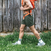Person wearing green shorts and white sneakers with green stripes, standing on grass against a wooden fence.