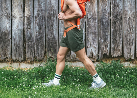 Person wearing green shorts and white sneakers with green stripes, standing on grass against a wooden fence.