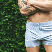 Shirtless man standing arms crossed in front of bush wearing gray slim fit boxer.