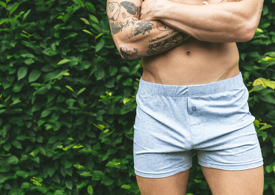 Shirtless man standing arms crossed in front of bush wearing gray slim fit boxer.