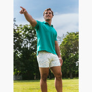 Man standing outside pointing wearing a green polo and white/purple pastel lounge shorts.