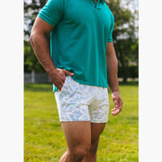 Close up shot of man standing outside wearing a green polo and white/purple pastel lounge shorts.