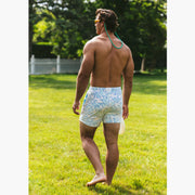 Shirtless man standing outside wearing a green polo and white/purple pastel lounge shorts.