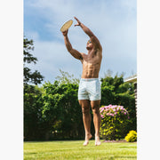 Shirtless man jumping outside wearing a green polo and white/purple pastel lounge shorts.