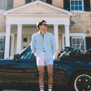 Man in pastel stripe slim fit boxers and tech varsity socks leaning on vintage car in front of house.