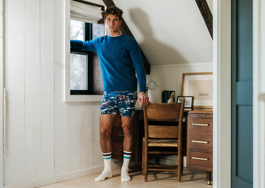 Man standing in bedroom wearing navy blue crewneck and navy slim fit boxers with horses, trees, and clouds.
