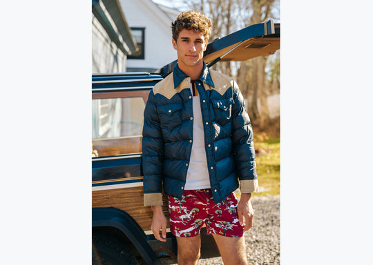 Man standing in front of wagoneer wearing blue jacket and red slim fit boxers with horses, clouds, and trees printed on.