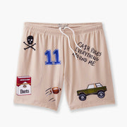 Beige lounge short that says "cash rules everything around me" with various icons like 11 patch, truck, football, skull and bones etc sitting flat with grey background. 