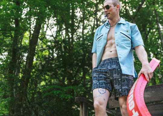 Man wearing sunglasses, blue polo, and black "schooner" mesh lounge shorts and he is holding a lifeguard floatie. 