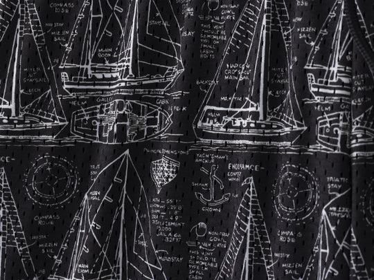 Close up detail shot of "Schooner" mesh lounge shorts that are black with white illustrations of boats.