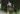 Shirtless man holding yellow paddle wearing blue mesh lounge shorts with merit badges printed on them.