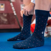 Man with both foot on the ground getting dressed wearing blue dot dress socks with initials "JBA" on one.