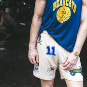 Man standing in doorway wearing blue basketball shirt and beige lounge short that says "cash rules everything around me" with various icons like 11 patch, truck, football, skull and bones etc. 