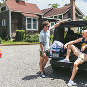 Two men outside by truck. One wearing grey shirt and olive short. The other wearing blue basketball shirt and Beige lounge short that says "cash rules everything around me" with various icons like 11 patch, truck, football, skull and bones etc. 