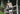 Shirtless man standing on porch of cabin wearing navy blue slim fit boxer and blue/white cap.