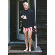 Man wearing black hoodie and red/cream stripe slim fit boxing standing outside front door holding coffee mug.