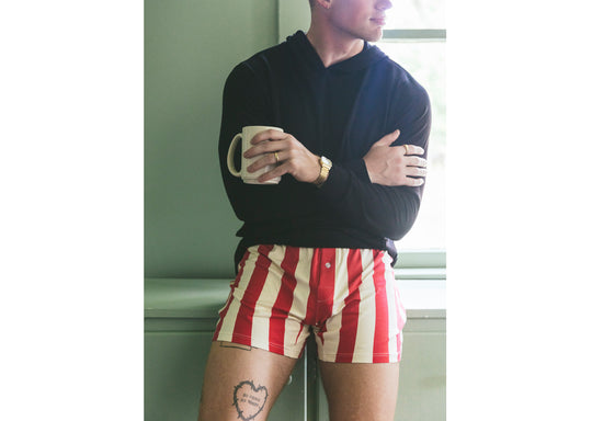 Man standing in kitchen holding a coffee mug wearing black sweatshirt and red/cream stripe slim fit boxer.