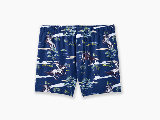 Pair of navy blue slim fit boxers with cowboys, trees and clouds printed on laid flat against grey background.